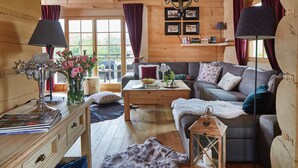 Un acogedor interior de cabaña con piso de madera, un sofá, una mesa con un jarrón de flores y una lámpara.