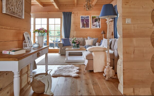 Interior acogedor de una cabaña con piso de madera, un conjunto de sofás, una mesa de comedor y una araña.
