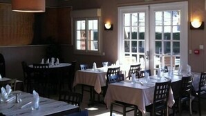 A restaurant with tables set for dining, large windows, and pendant lighting. - Storia Da Ennio (La Verriere)