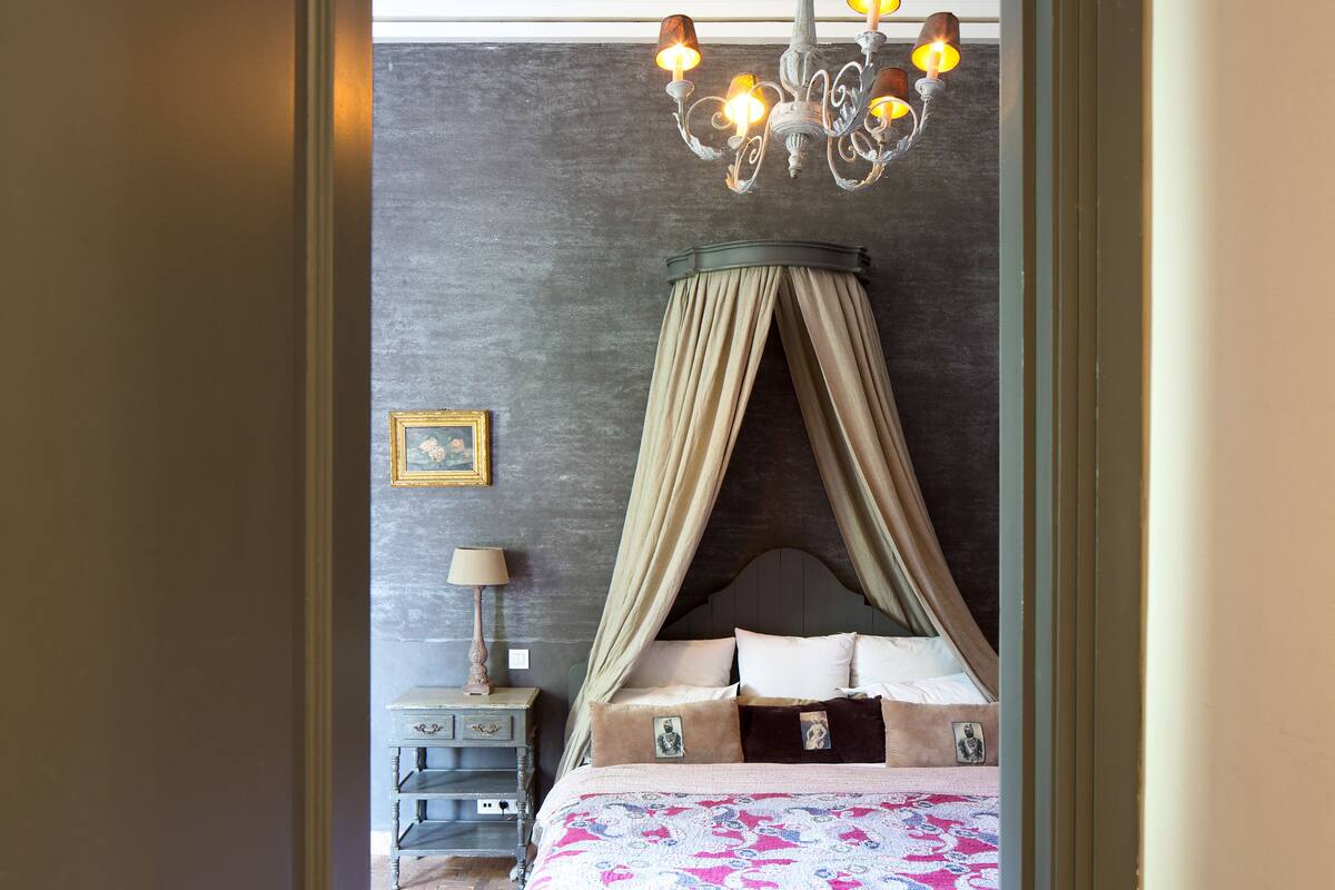 A bedroom with a canopy bed, a bedside table with a lamp, and a framed picture on the wall.