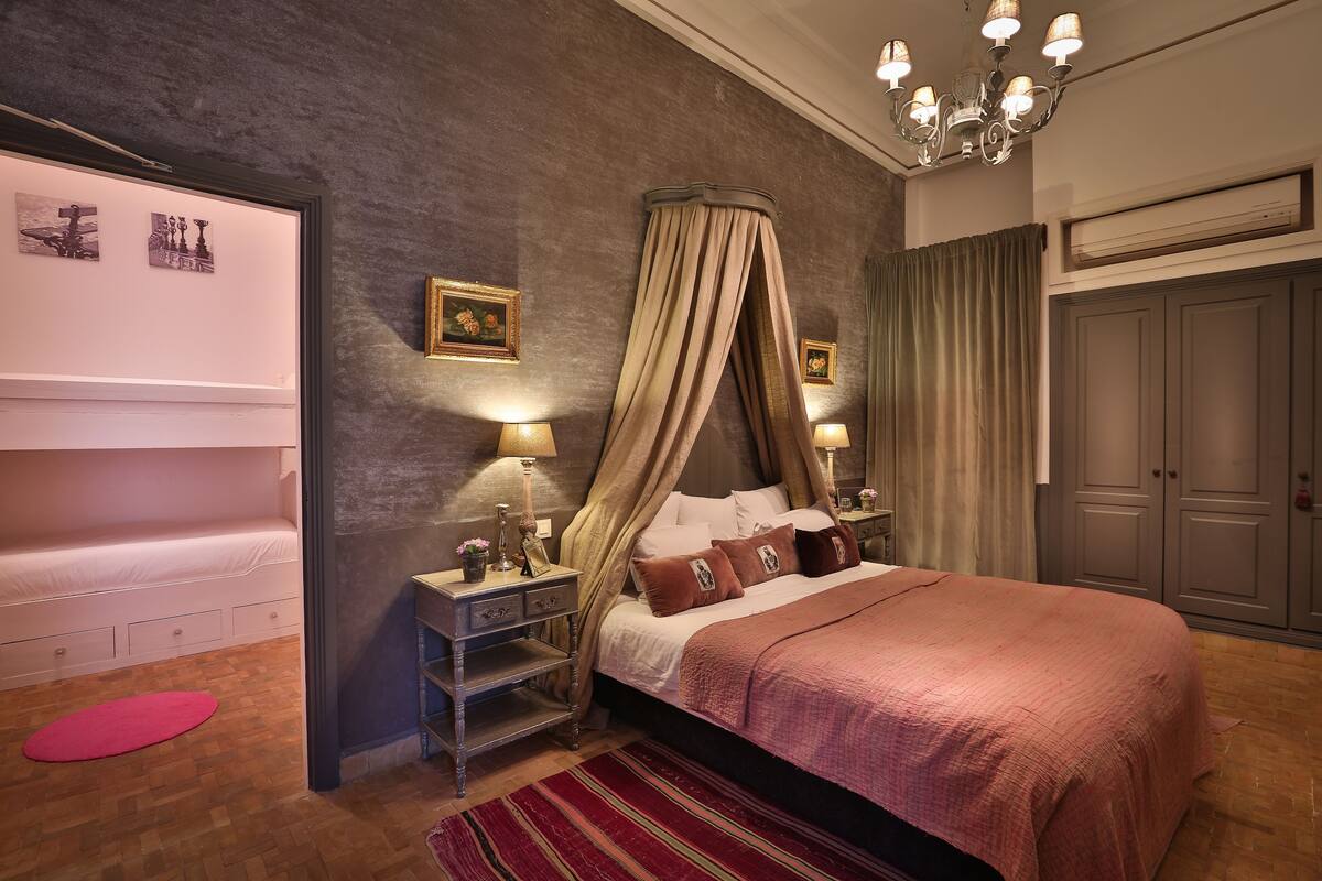 A bedroom with a canopy bed, bedside tables with lamps, a red rug, and a wardrobe.
