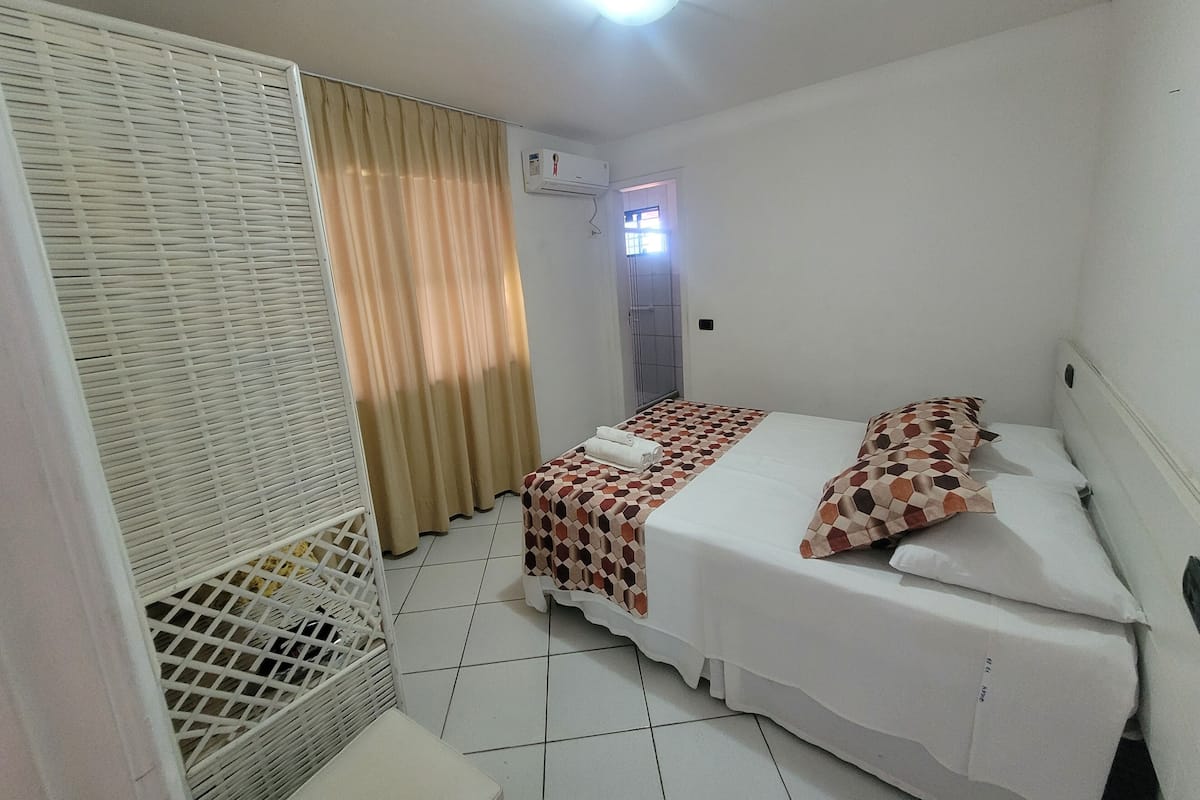 A small, clean room with a bed, a white wardrobe, and a window with curtains.