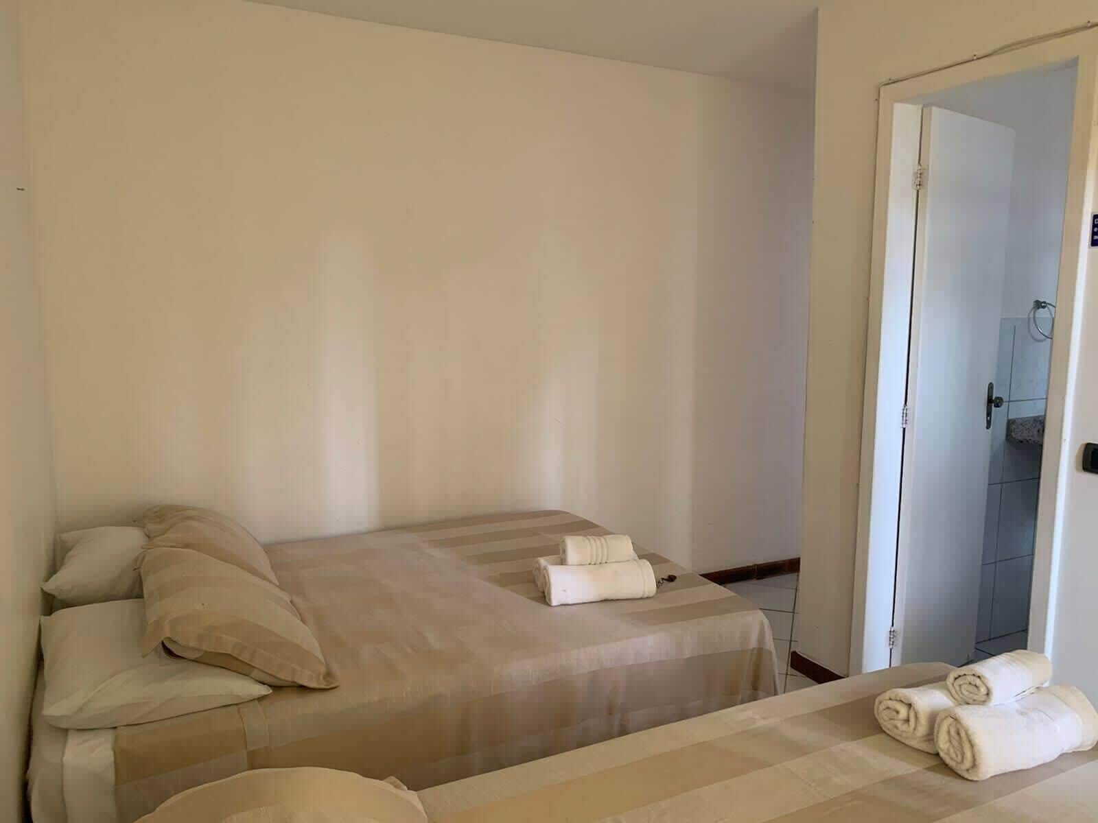 Een eenvoudige, nette kamer met een bed, een klein tafeltje en een badkamer die door een open deur zichtbaar is.