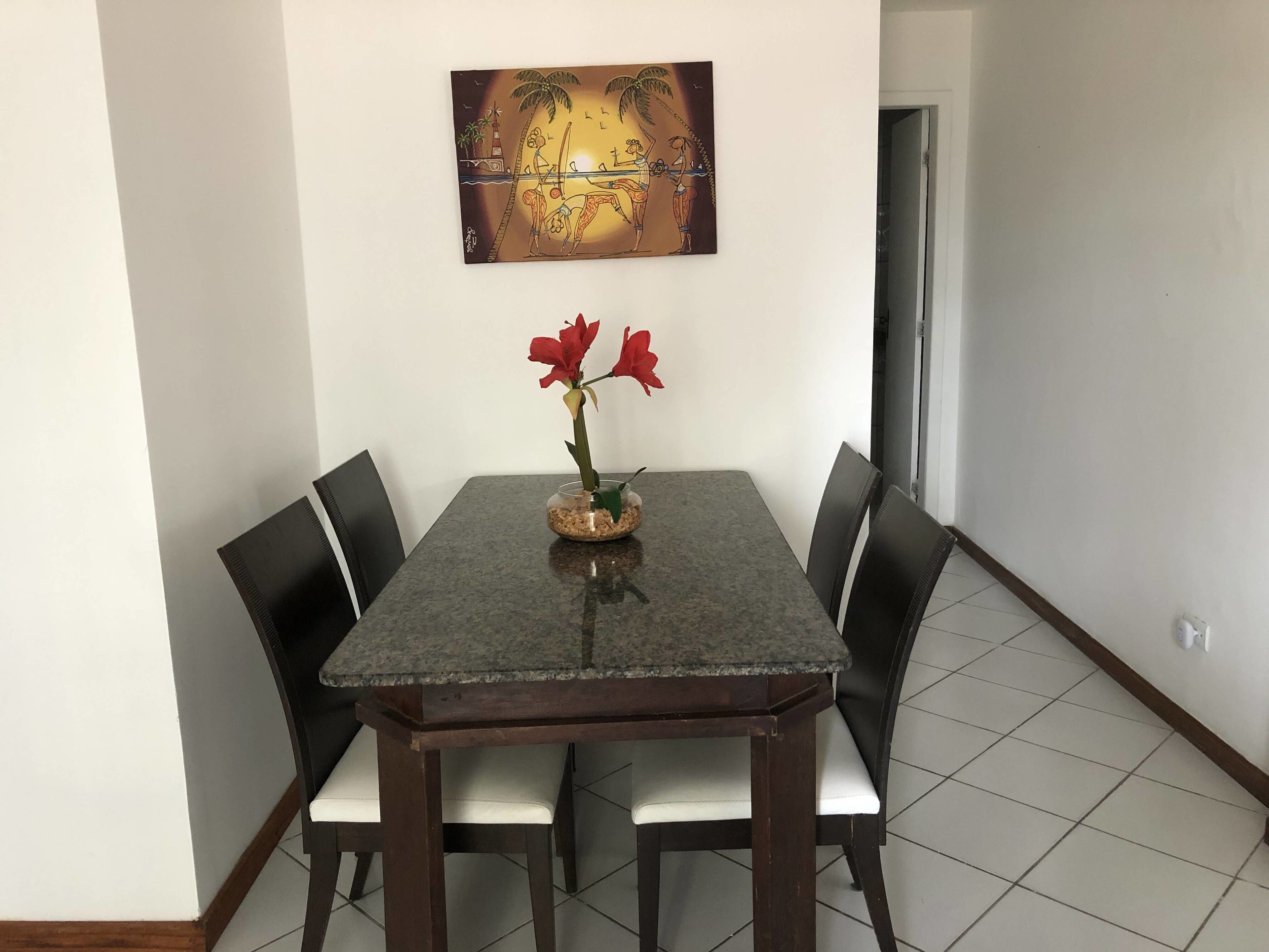 A dining area with a table, chairs, and a vase with red flowers.