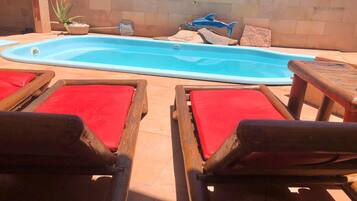 A swimming pool with a hot tub, surrounded by wooden lounge chairs with red cushions.