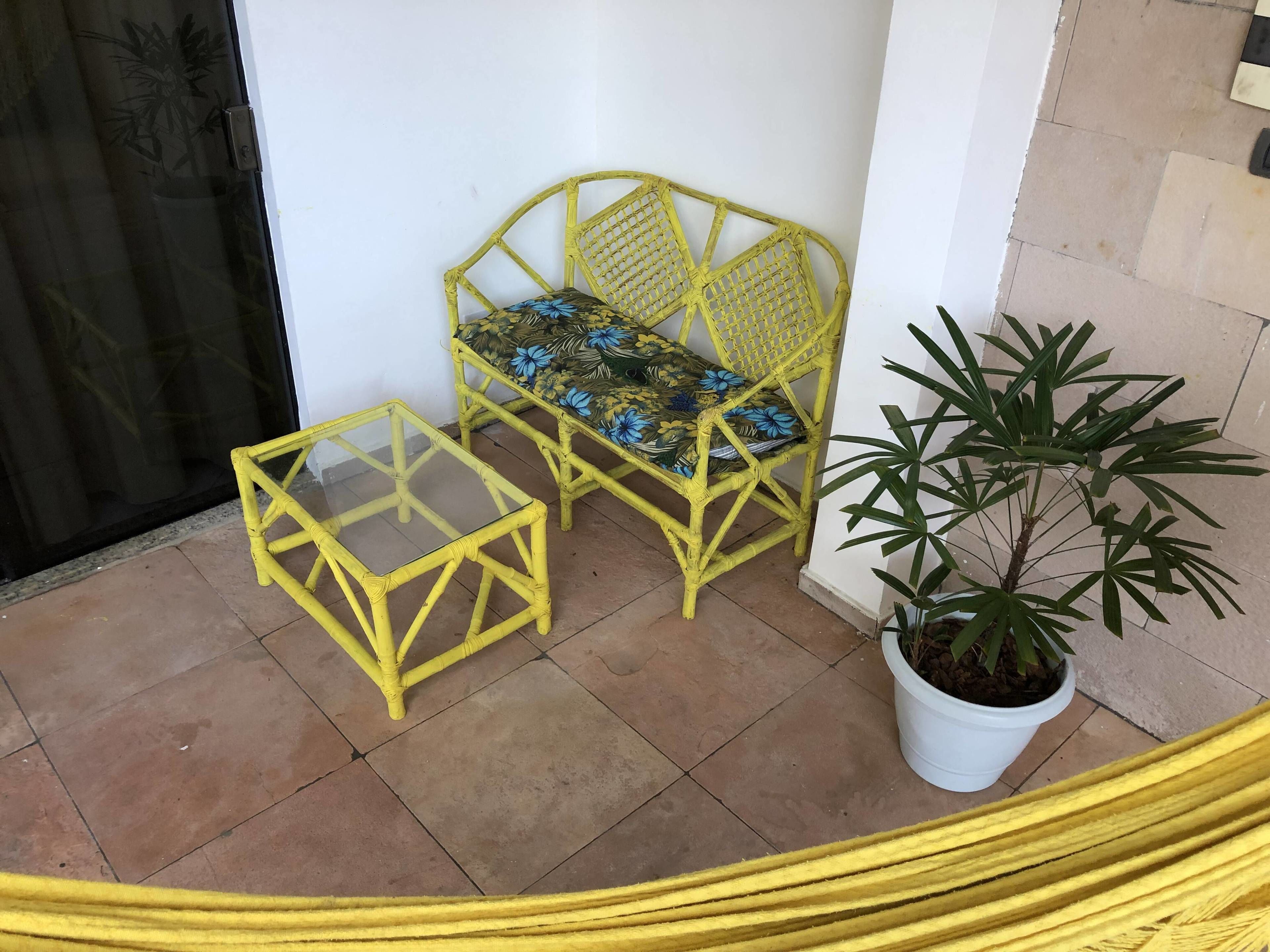 A yellow rattan chair and table set on a tiled patio, with a potted plant nearby.