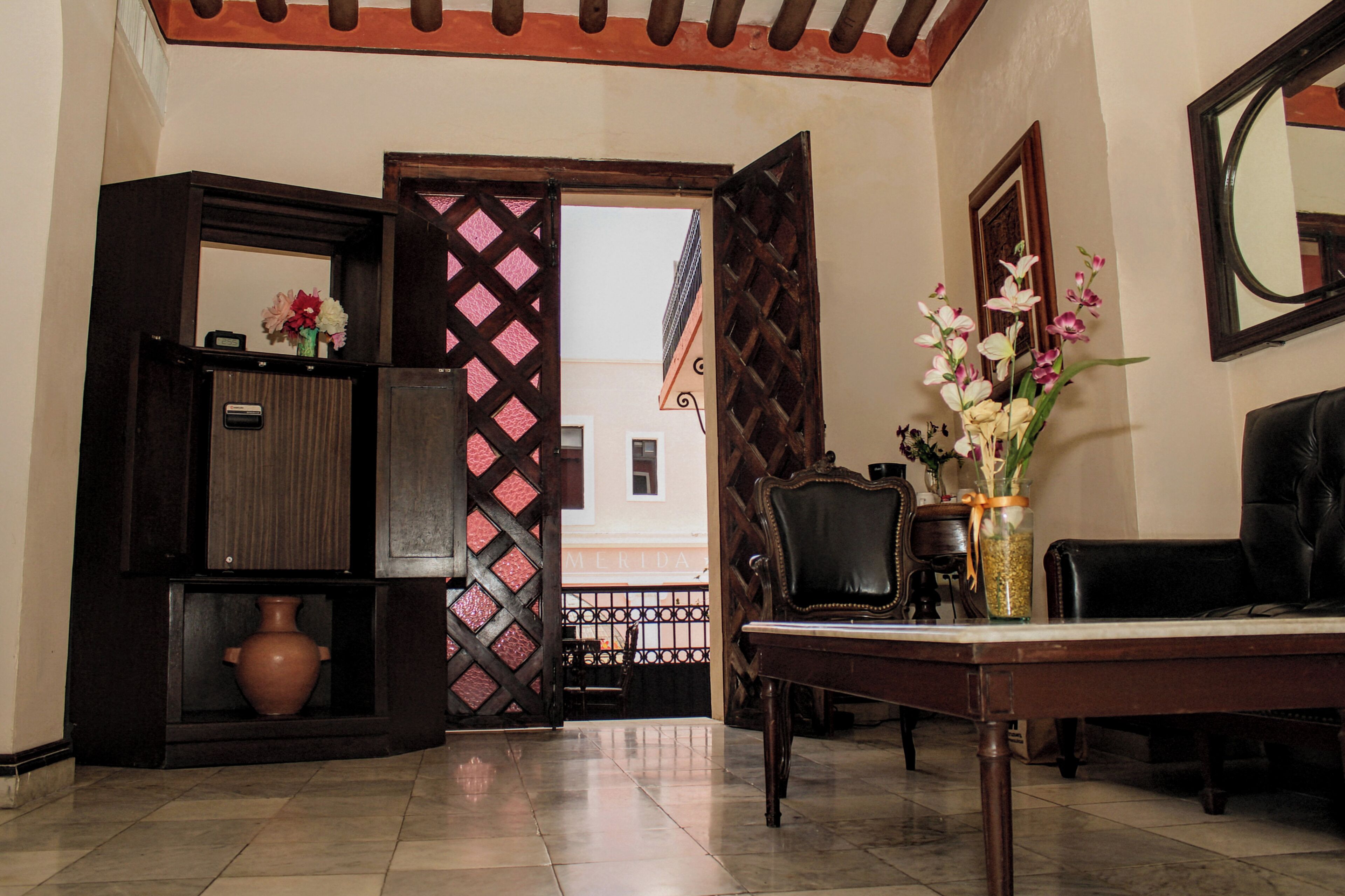 Un vestíbulo con un mostrador de recepción de madera, un sofá de cuero negro, un jarrón con flores y un espejo grande en la pared.