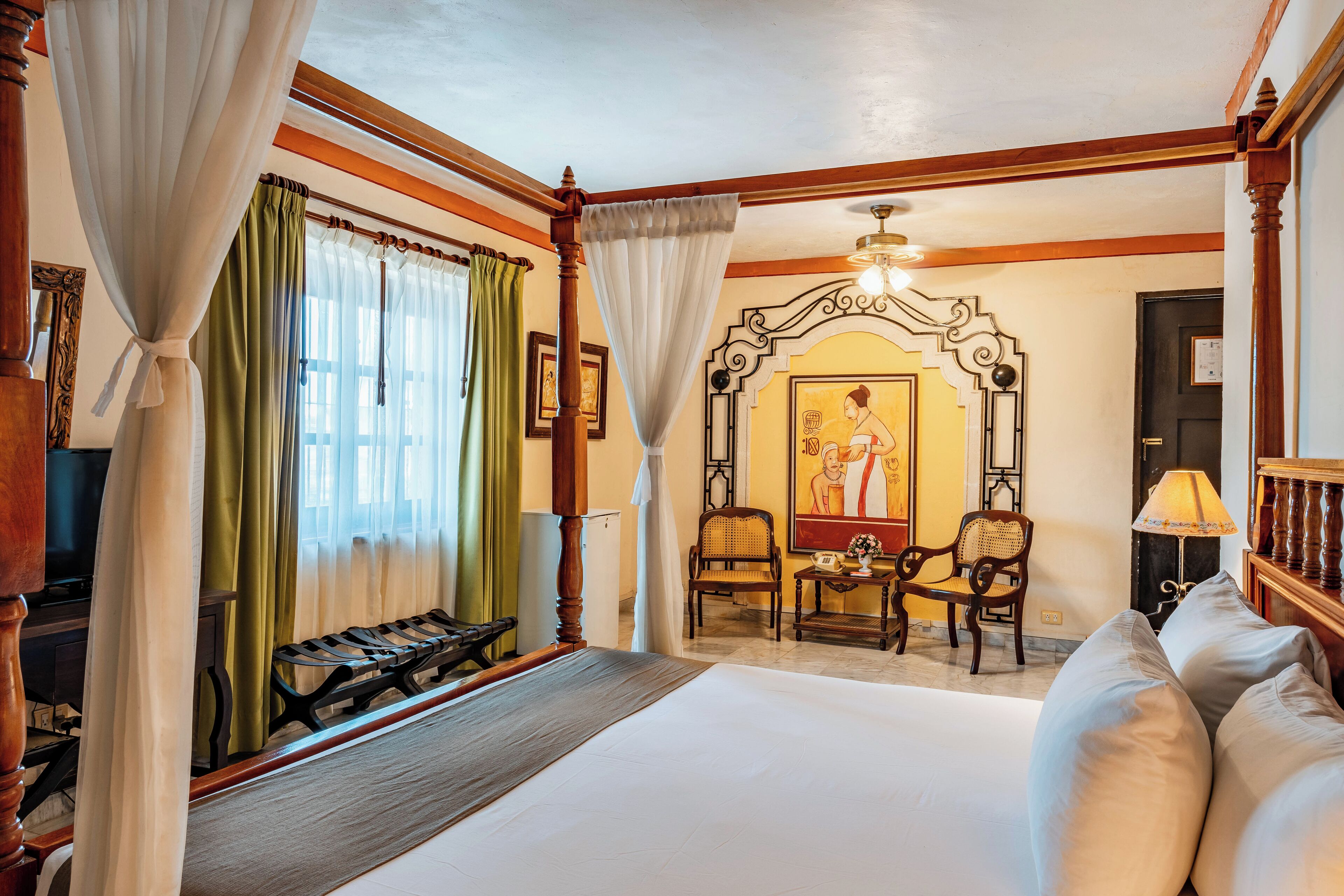 Une chambre d’hôtel avec un grand lit, un banc en bois, deux chaises, une table et un tableau au mur.