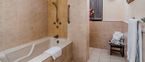 A bathroom with a bathtub, a shower, and a small table with towels.