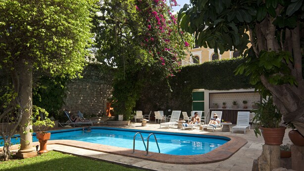 A swimming pool with lounge chairs and a stone wall in the background. - Casa del Balam Merida (Mérida)