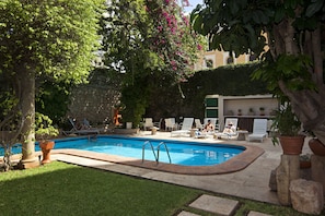 A swimming pool with lounge chairs and a stone wall in the background. - Casa del Balam Merida (Mérida)