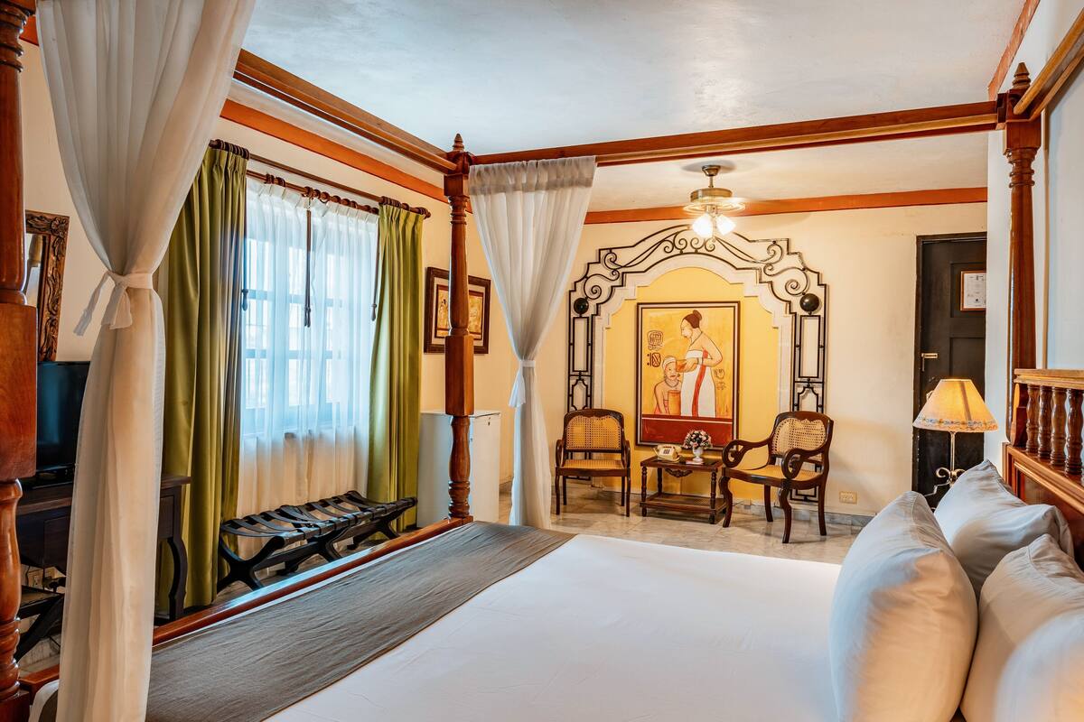 A hotel room with a bed, a desk, two chairs, a television, and a painting on the wall.