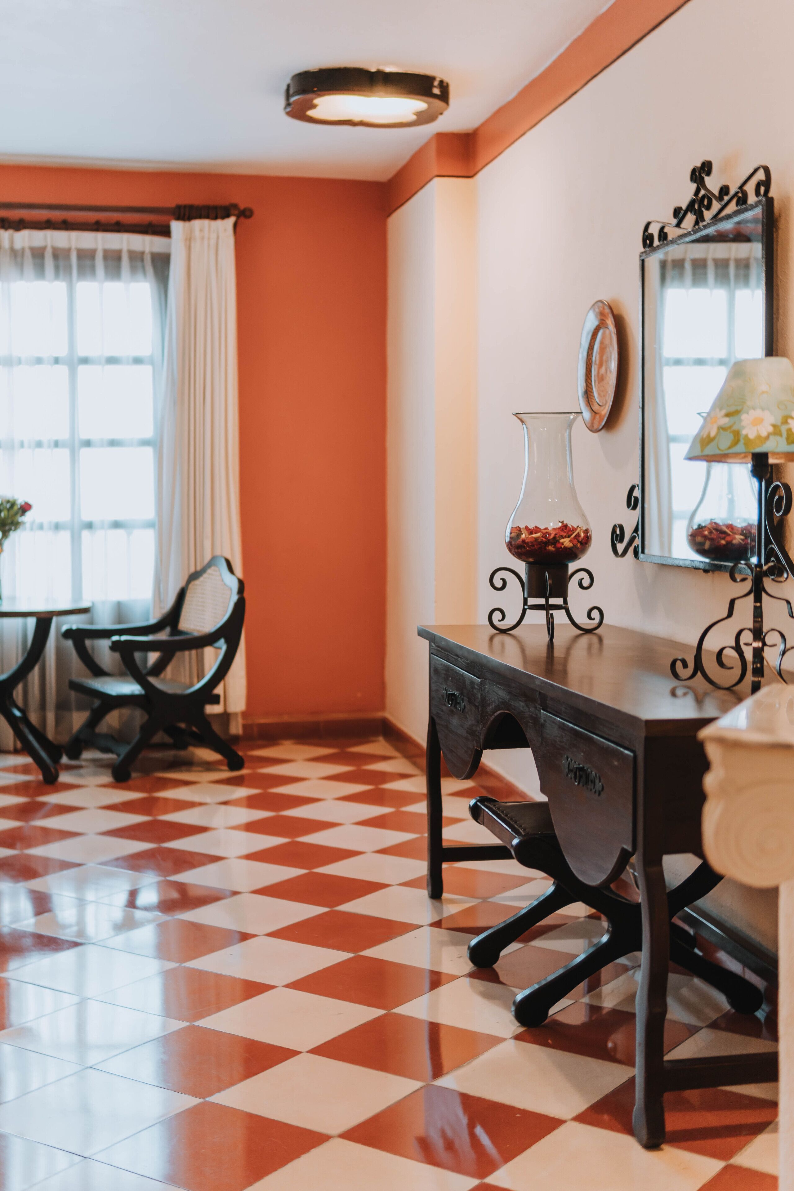 Una habitación con suelo a cuadros, una mesa con sillas, un jarrón con flores, una lámpara y un espejo en la pared.
