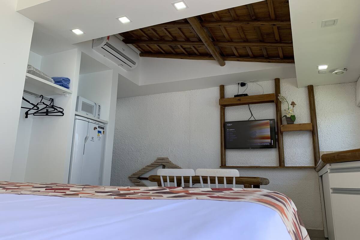 A compact room with a bed, a small desk, a TV, and a wooden ceiling.