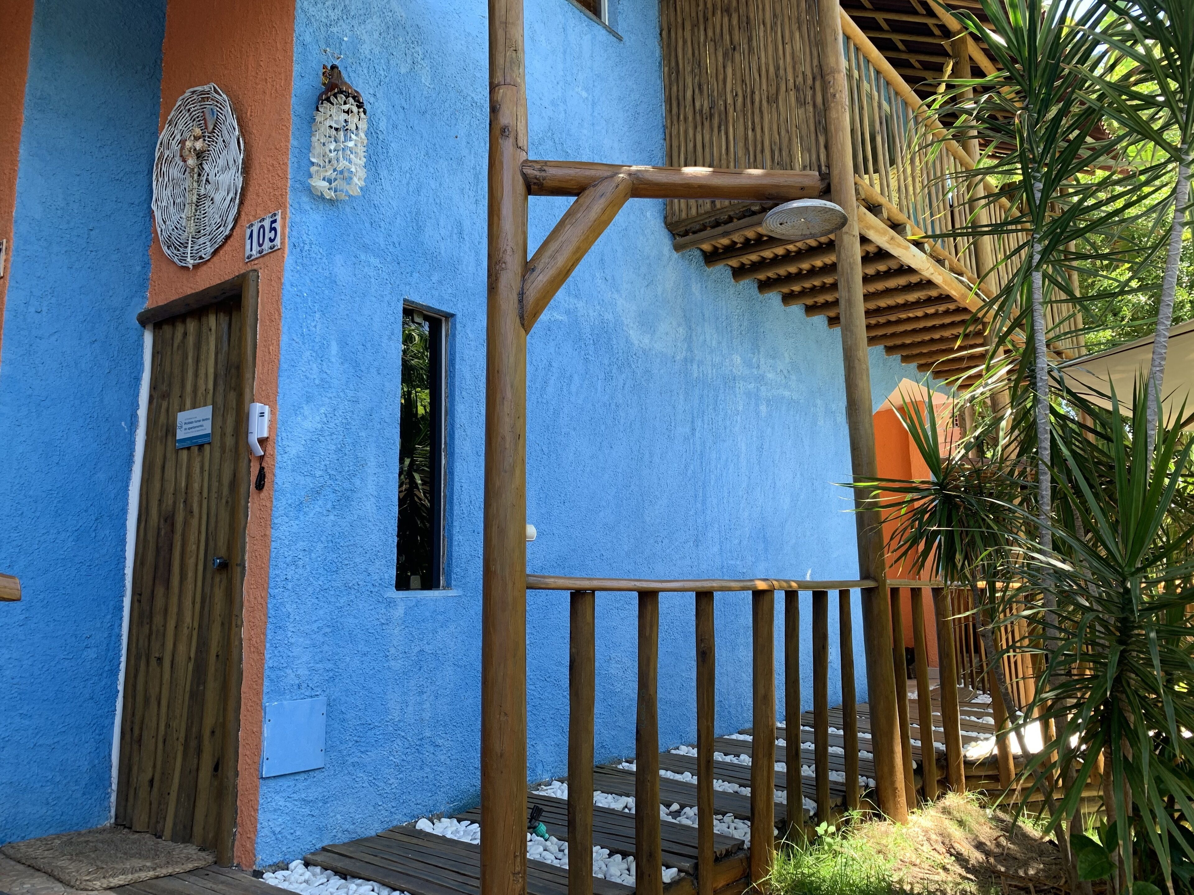 Um edifício azul com porta e janela de madeira, escada de madeira e estrutura de bambu.
