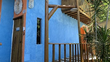 Um edifício azul com porta e janela de madeira, escada de madeira e estrutura de bambu.