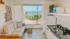 A modern living room with a sofa, a hammock, a TV, and a kitchen area with a sink and a refrigerator. - Villaggio Orizzonte (Salvador)