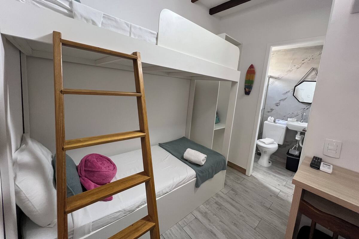 A bunk bed room with a wooden ladder, a small table, and a bathroom with a mirror and sink.