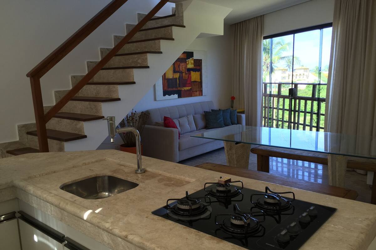 A kitchen with a gas stove, a sink, and a staircase leading to another level.
