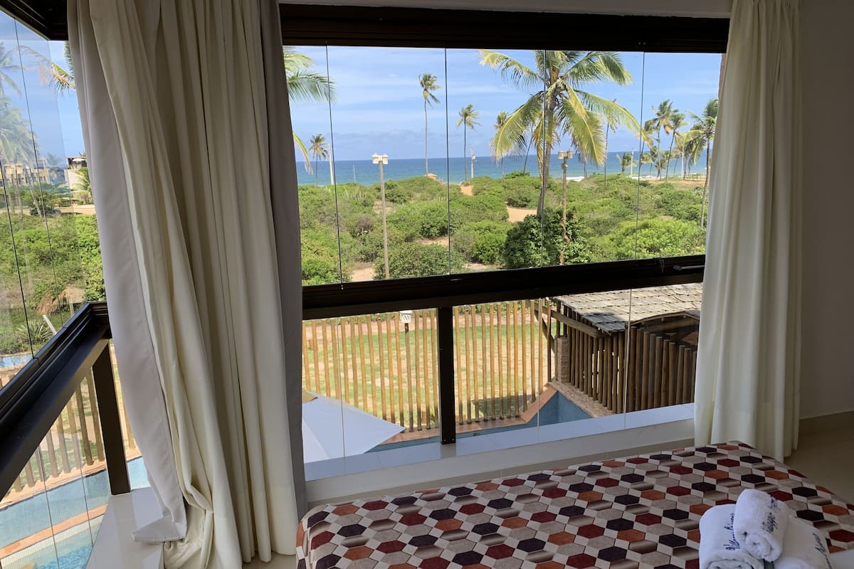 A hotel room with a bed, a view of a beach, and a pool.