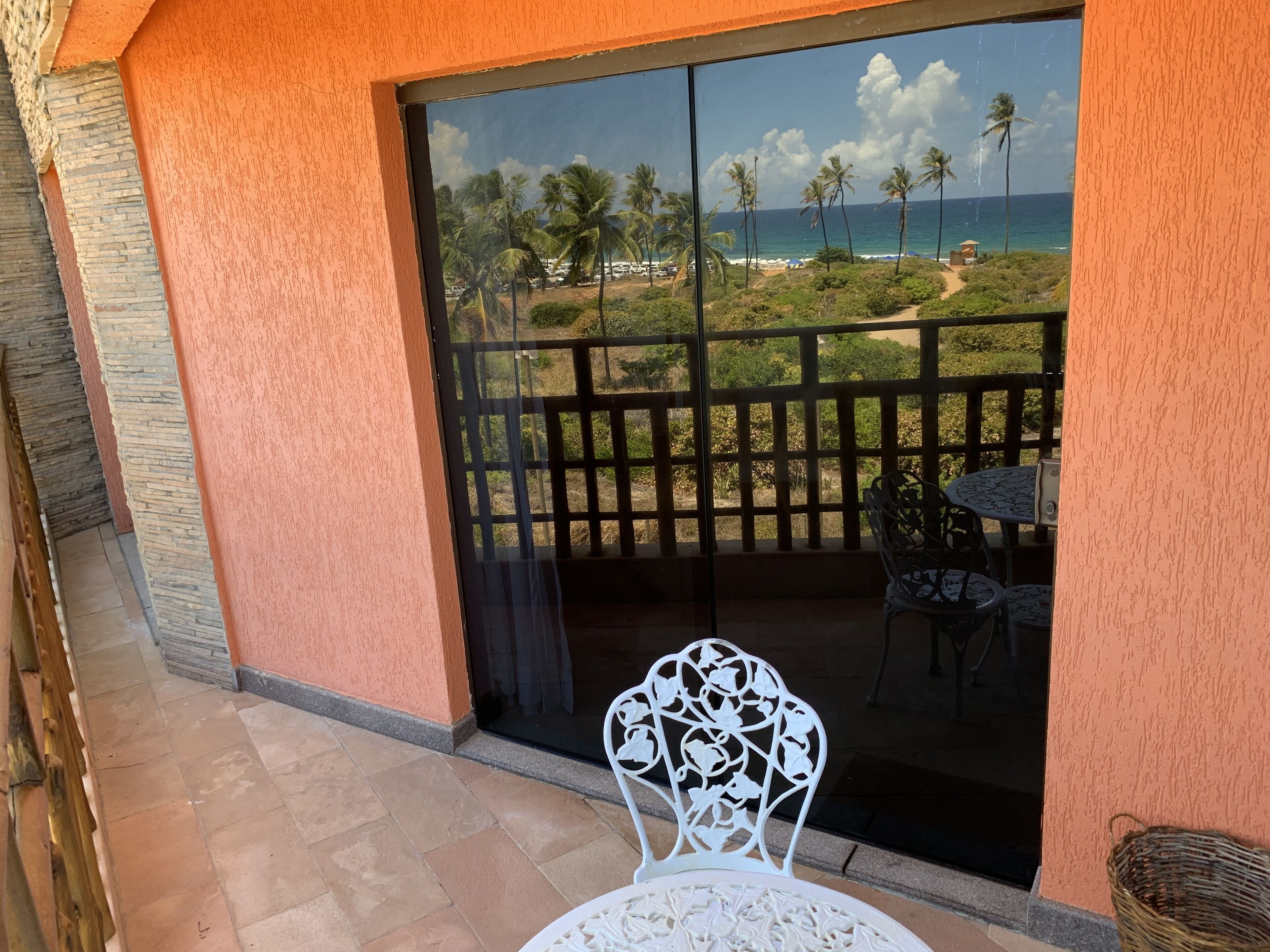 A balcony with a view of the beach, a table, and a chair.