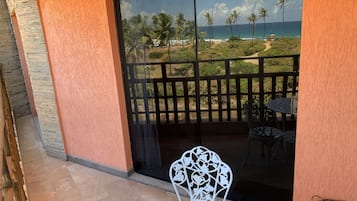 A balcony with a view of the beach, a table, and a chair.