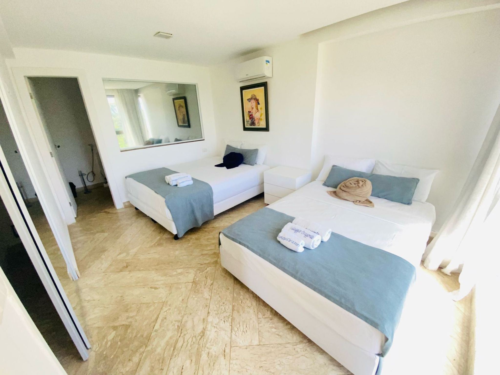 Una habitación de hotel con dos camas, una zona de estar, un espejo grande y un cuadro en la pared.