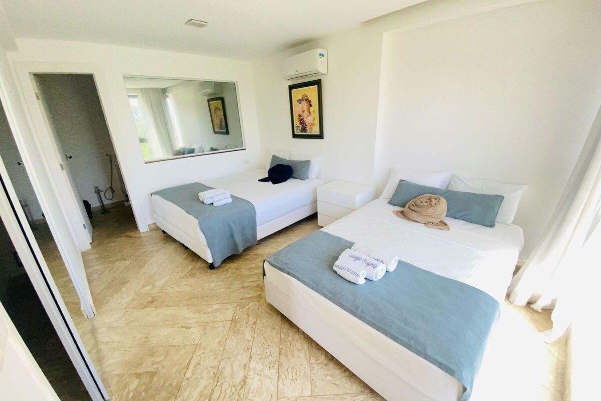 A hotel room with two beds, a sitting area, a large mirror, and a painting on the wall.