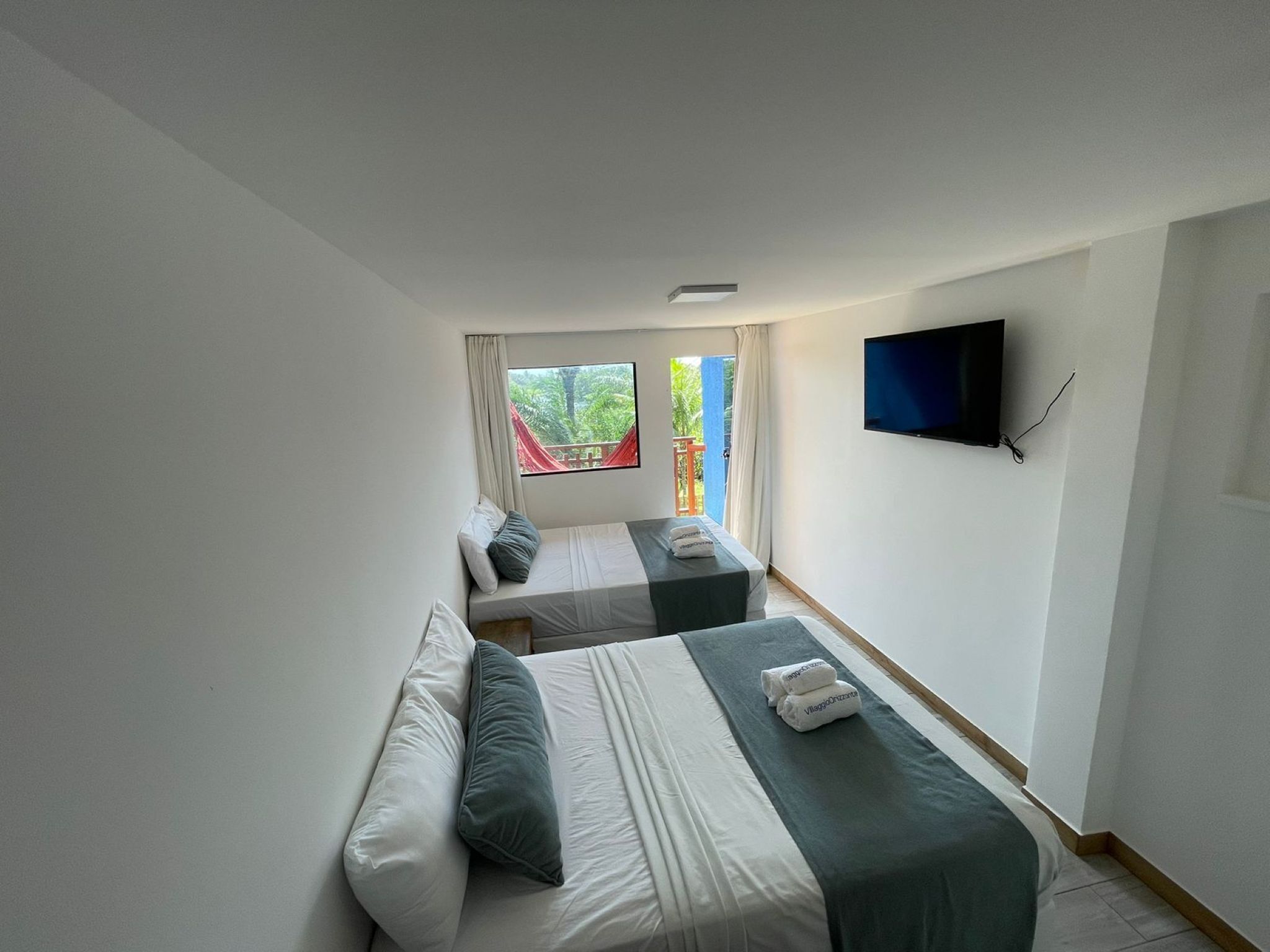 Habitación de hotel con dos camas, televisión y ventana con vista a vegetación.