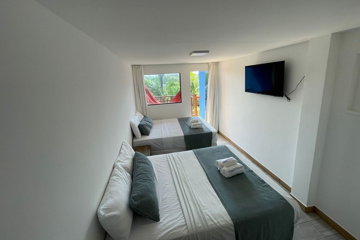 A hotel room with two beds, a TV, and a window with a view of greenery.