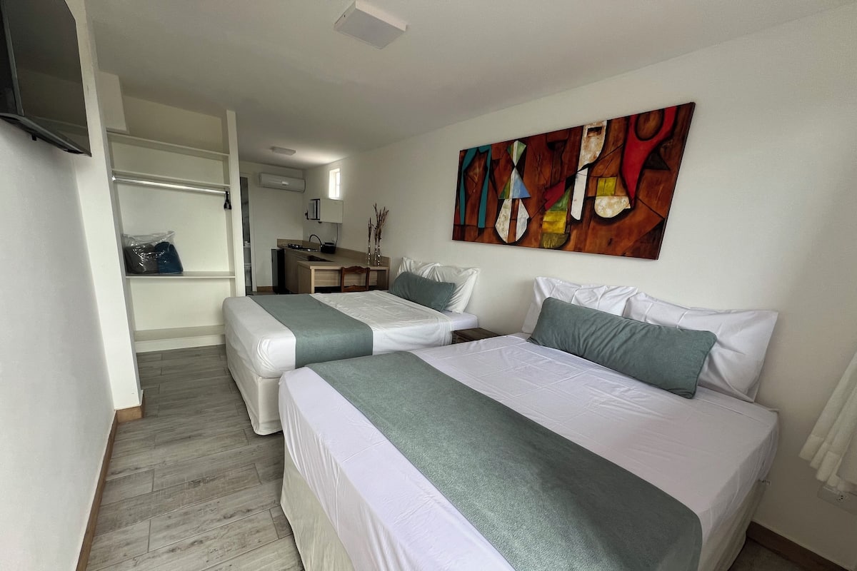 A hotel room with two beds, a desk, and a kitchenette.