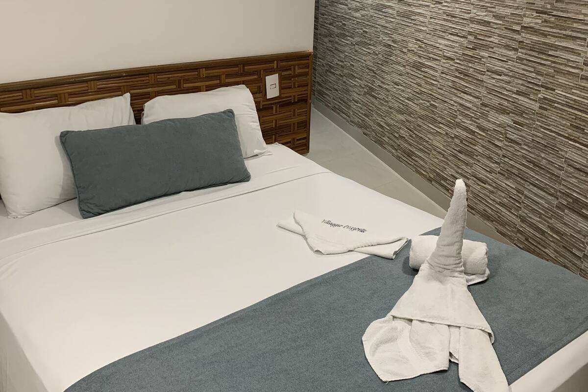 A hotel room with a bed, a wooden headboard, a textured wall, and an air conditioning unit.