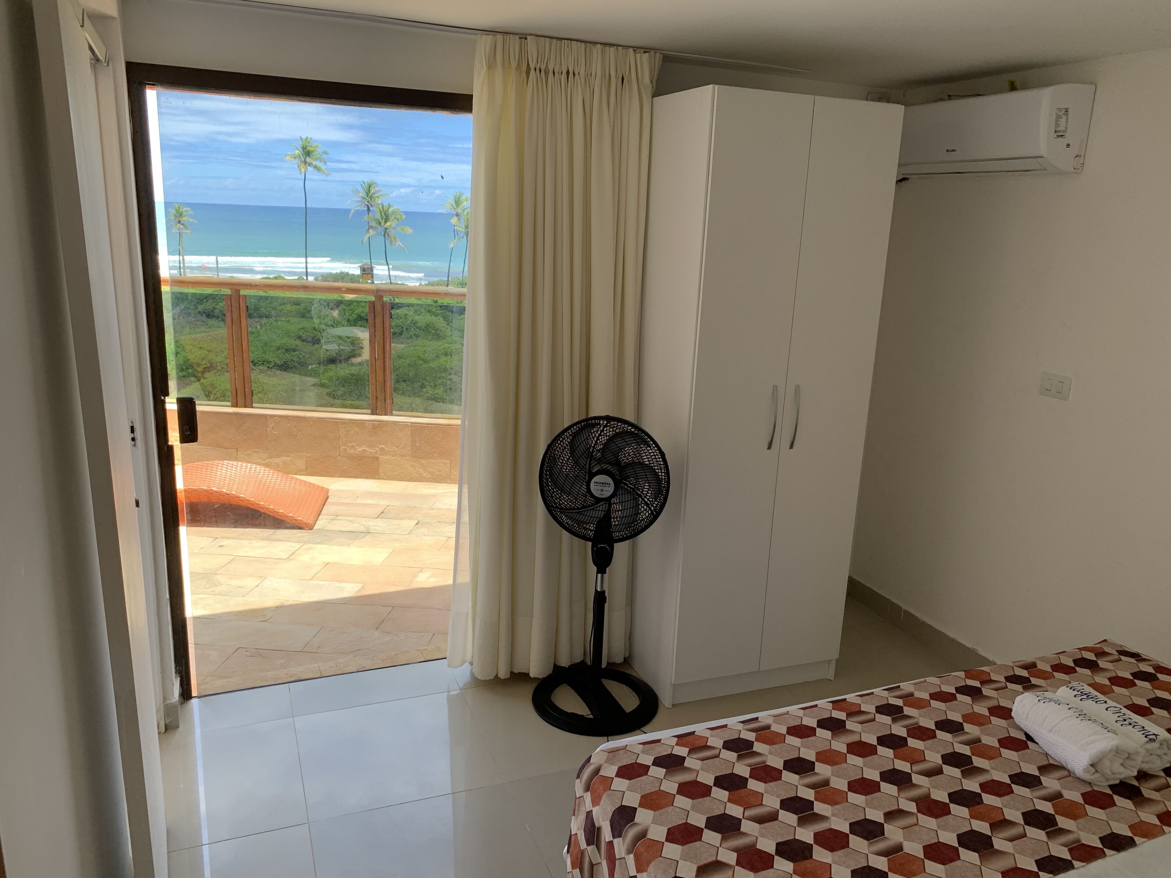 Un dormitorio con cama, ventilador, armario y vista al océano.
