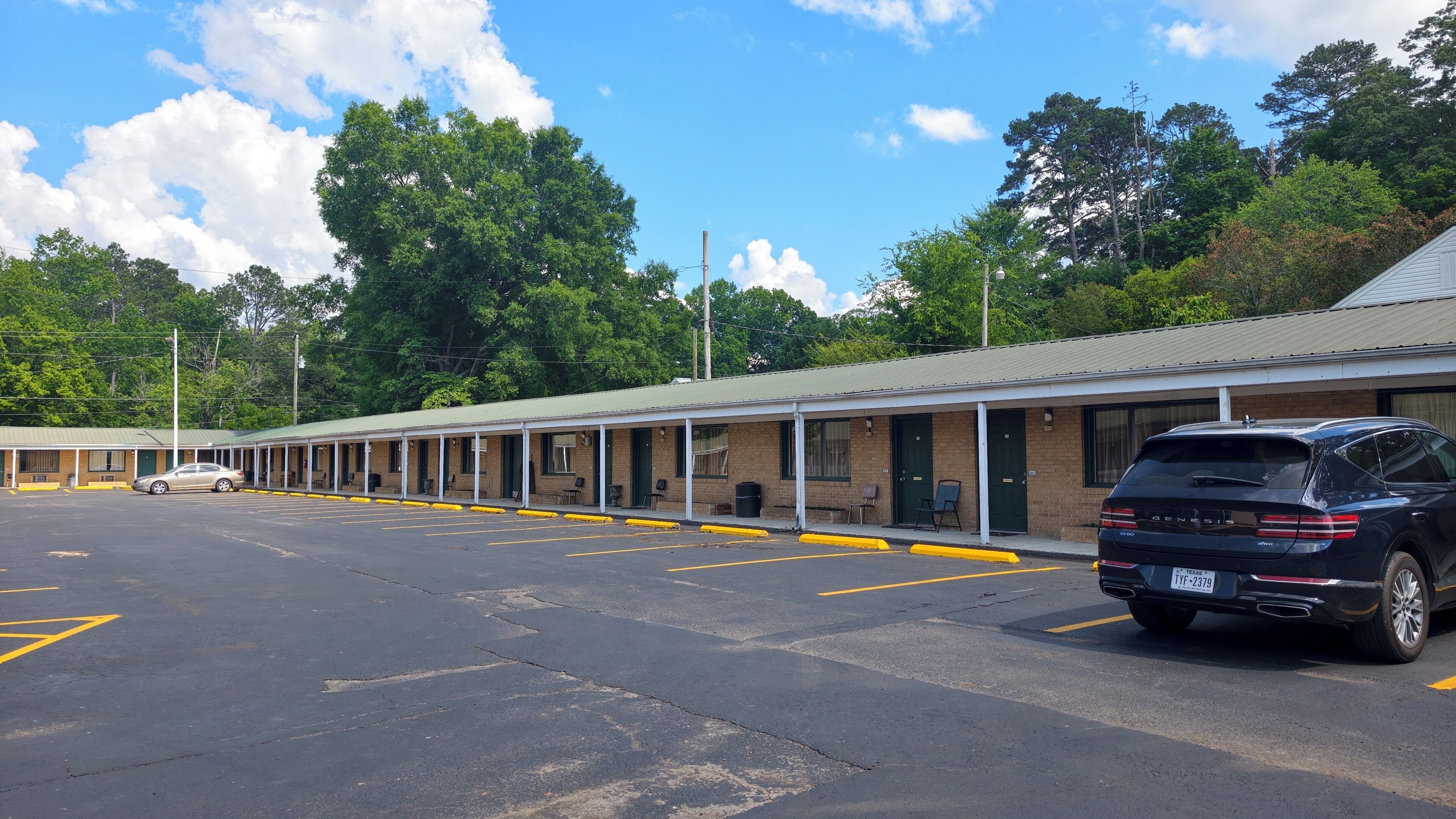Ein Motel mit einer Reihe von Zimmern, einem Parkplatz und Bäumen im Hintergrund.