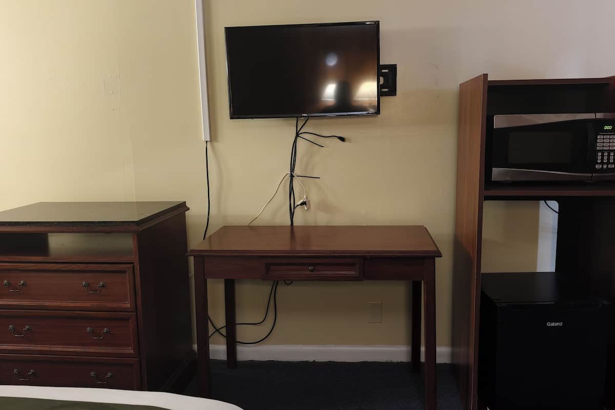 A room with a wooden desk, a television mounted on the wall, and a microwave shelf.