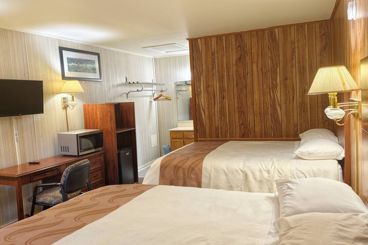 A hotel room with two beds, a desk with a microwave, a TV, and a wooden panel wall.