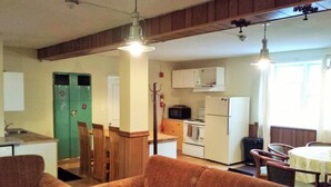 Eine kleine Küche mit Mikrowelle, Herd und Kühlschrank. Holzstühle und ein Esstisch mit gelber Tischdecke sind vorhanden.