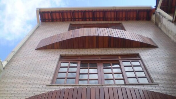A building with a brick facade, a large window with multiple panes, and a curved wooden structure at the bottom. - Albergue Rio Vermelho - Hostel (Salvador)