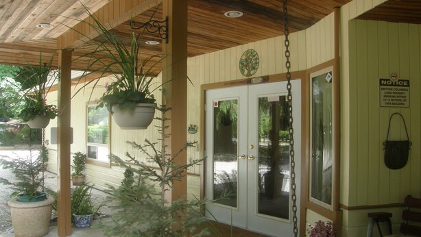 A wooden porch with hanging planters and a door with a notice sign. - Cedar Wood Lodge B&B (Port Alberni)