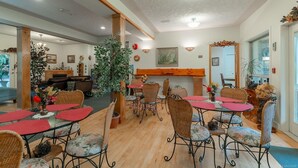 A dining area with wicker chairs and red tablecloths, a wooden bench, and a large potted plant. - Cedar Wood Lodge B&B (Port Alberni)