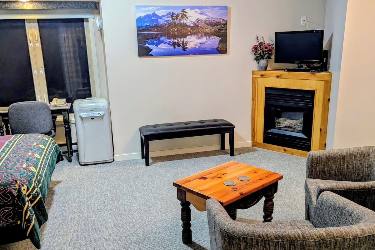A living room with a ceiling fan, a fireplace, a television, a bench, and a painting on the wall.