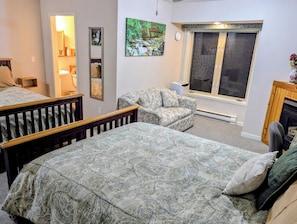 Una habitación con una cama, una silla, un ventanal, un espejo y un cuadro.