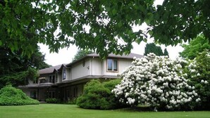 A two-story house with a well-maintained lawn and a large flowering bush in the foreground. - Cedar Wood Lodge B&B (Port Alberni)