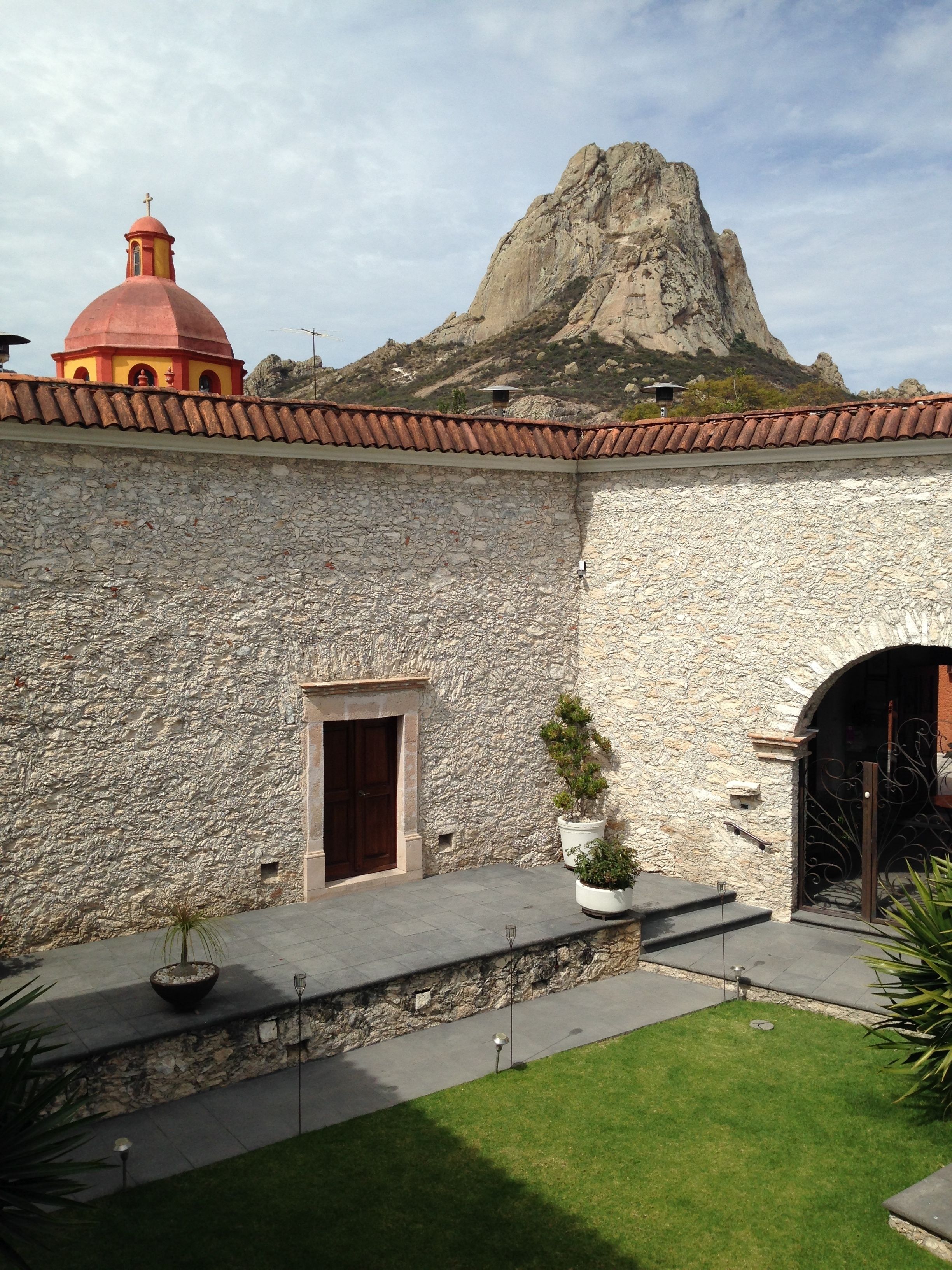 A courtyard with a stone wall, a red dome, and a mountain in the background.