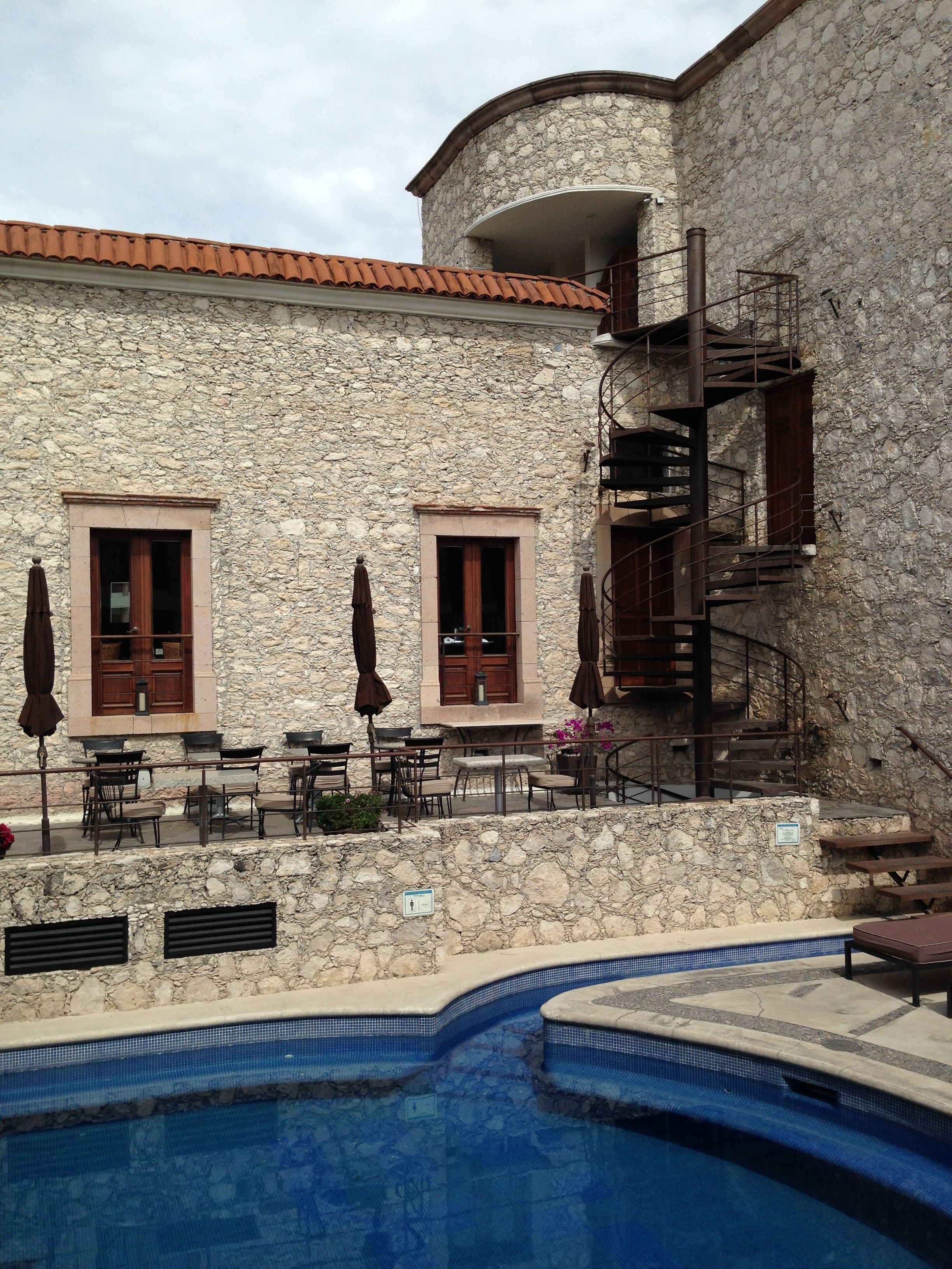 A stone building with a pool, outdoor seating, and a spiral staircase.