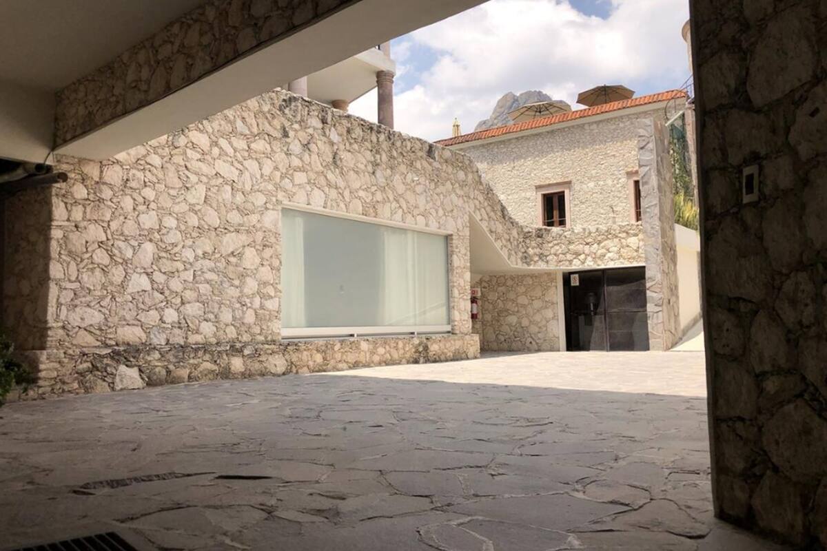 A stone building with a large window and a door, set in a courtyard with stone paving.