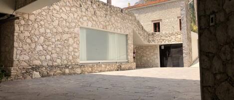 A stone building with a large window and a door, set in a courtyard with stone paving.