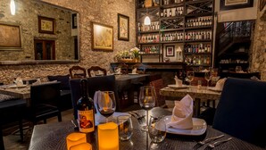 A restaurant interior with stone walls, framed artwork, and a wine rack. Tables are set with candles, wine glasses, and cutlery. - Hotel Boutique Casa Mateo (Ezequiel Montes)