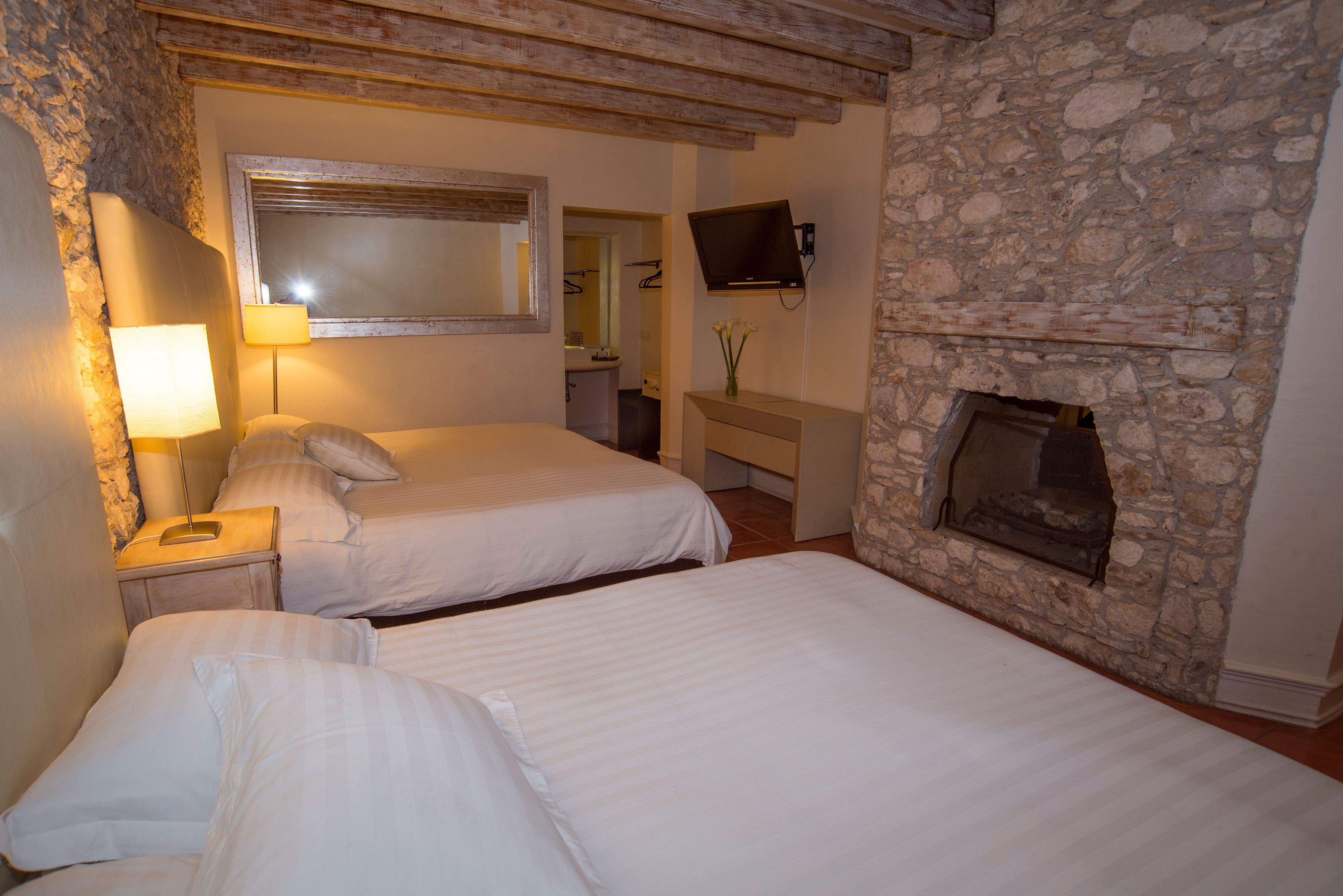 Ein Schlafzimmer mit zwei Betten, einem Kamin aus Stein, einem angebrachten Fernseher und einem Spiegel an der Wand.