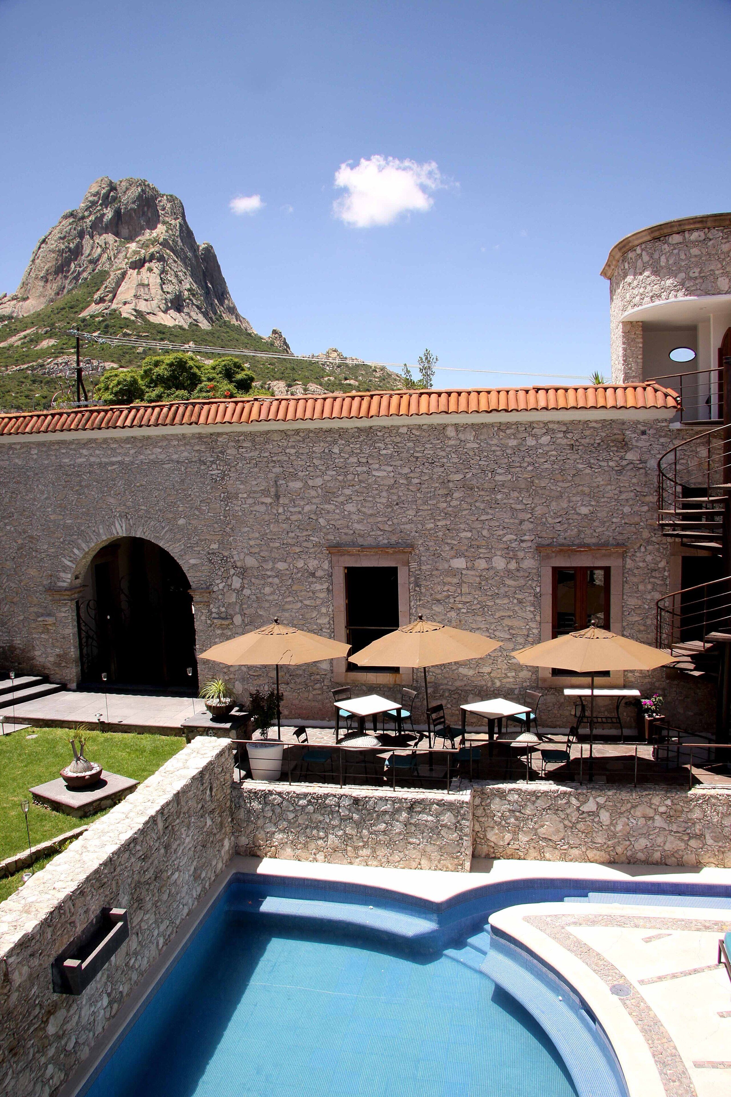A stone building with a swimming pool, outdoor seating, and a mountain in the background.